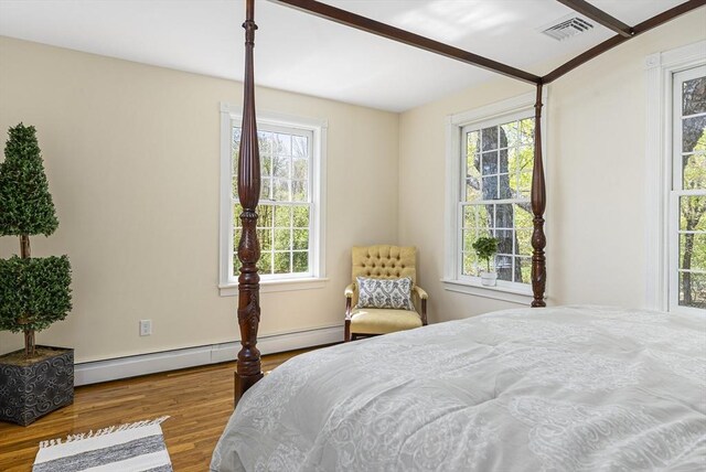 bedroom with a baseboard heating unit, multiple windows, and wood-type flooring