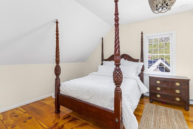 bedroom featuring vaulted ceiling, a baseboard radiator, and light wood-type flooring