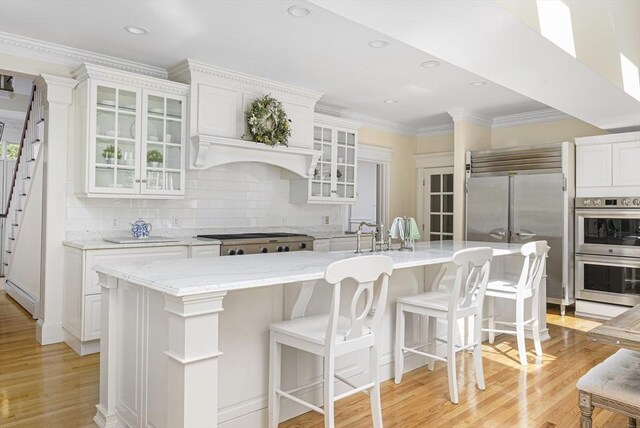 kitchen featuring light hardwood / wood-style floors, tasteful backsplash, an island with sink, stainless steel appliances, and white cabinets