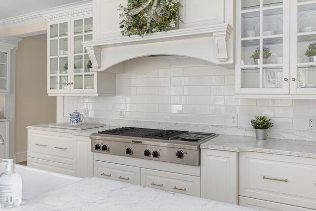 kitchen with stainless steel gas stovetop, light stone counters, backsplash, and white cabinetry