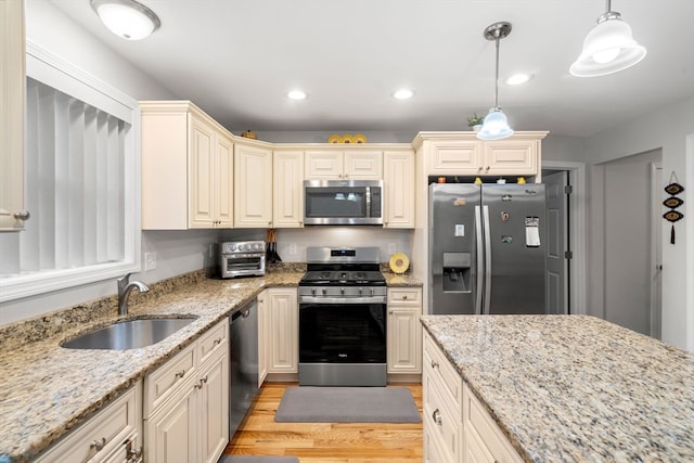 kitchen with appliances with stainless steel finishes, decorative light fixtures, light stone countertops, sink, and light hardwood / wood-style flooring