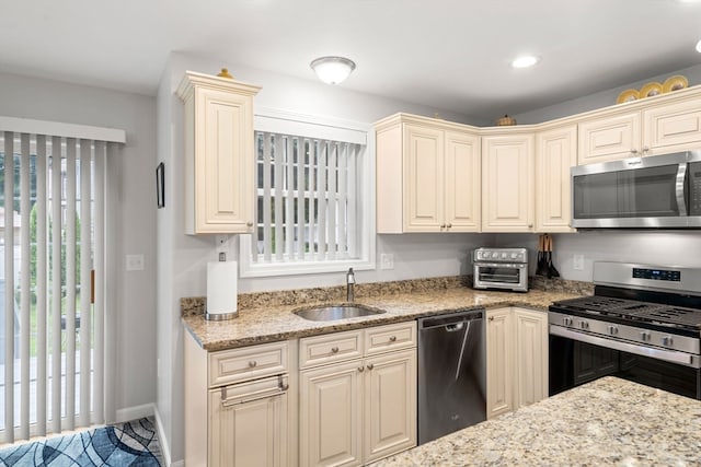 kitchen featuring light stone countertops, cream cabinetry, sink, and appliances with stainless steel finishes