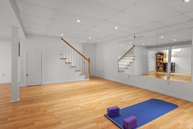 exercise room with baseboards, a drop ceiling, and light wood finished floors