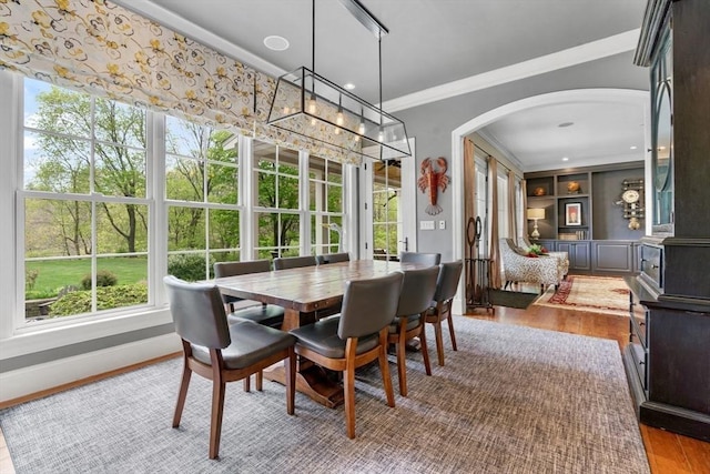 dining area with crown molding, arched walkways, baseboards, and wood finished floors