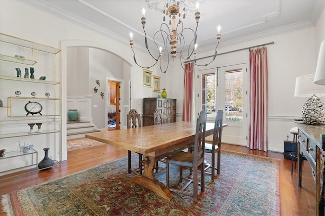 dining room with arched walkways, a chandelier, stairs, wood finished floors, and ornamental molding