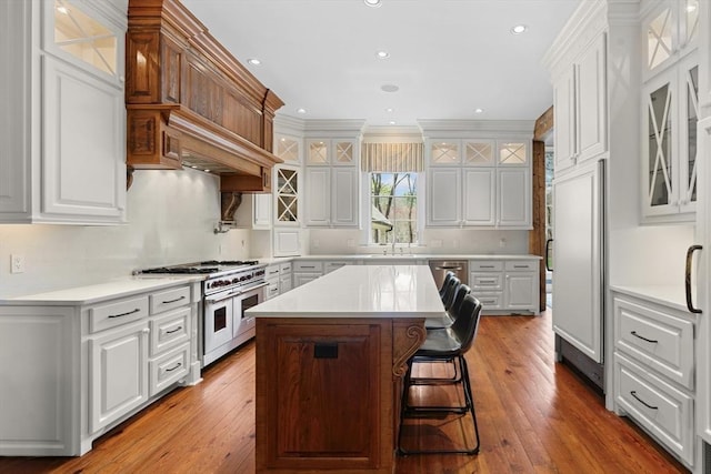 kitchen featuring light countertops, white cabinets, high end appliances, and hardwood / wood-style floors