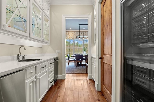 bar featuring dishwasher, a sink, baseboards, wood-type flooring, and ornamental molding