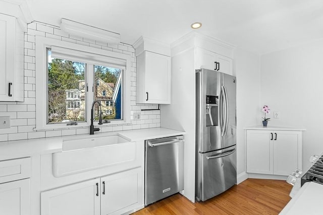 kitchen with appliances with stainless steel finishes, a sink, light wood-style floors, light countertops, and backsplash