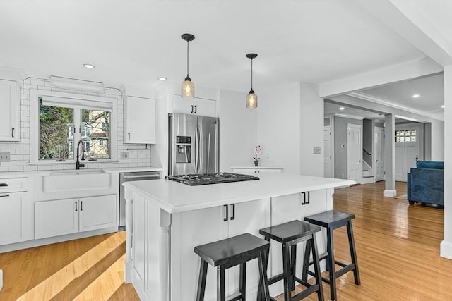 kitchen featuring appliances with stainless steel finishes, a sink, light countertops, a center island, and tasteful backsplash