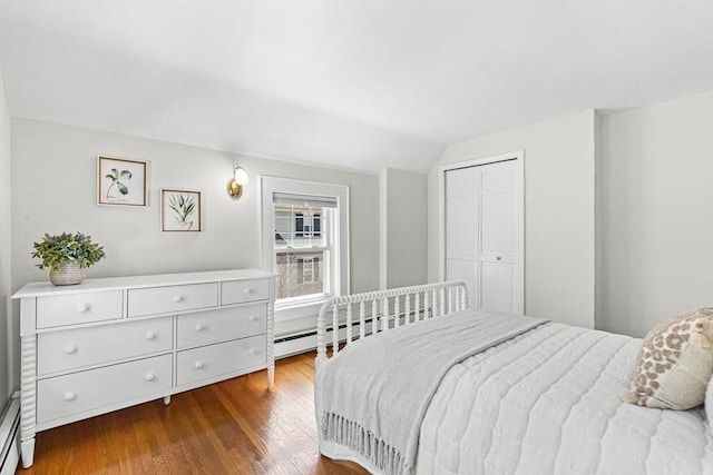 bedroom with a closet, dark wood finished floors, lofted ceiling, and a baseboard heating unit