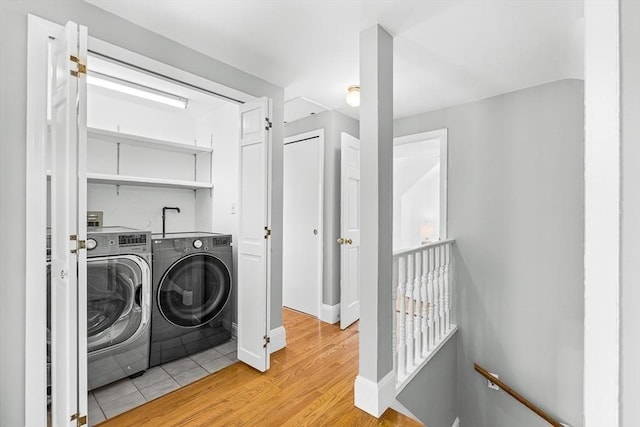clothes washing area with baseboards, light wood-style flooring, and washer and dryer