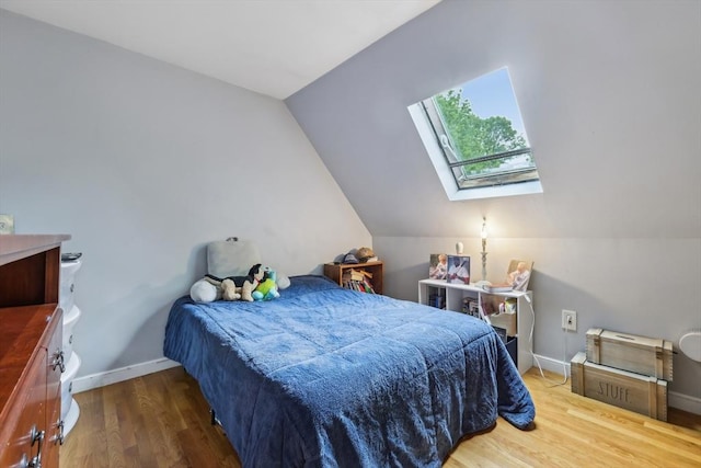 bedroom with baseboards, vaulted ceiling with skylight, and wood finished floors