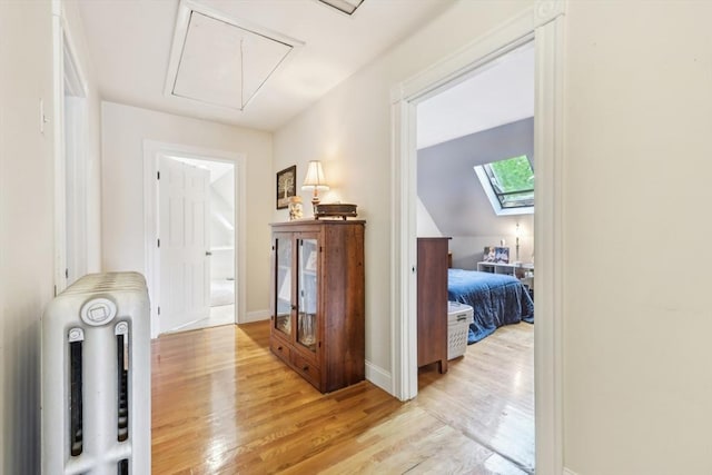 hall with a skylight, radiator, attic access, light wood-style flooring, and baseboards