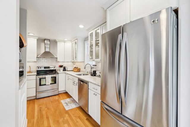 kitchen with a sink, stainless steel appliances, tasteful backsplash, wall chimney exhaust hood, and white cabinetry