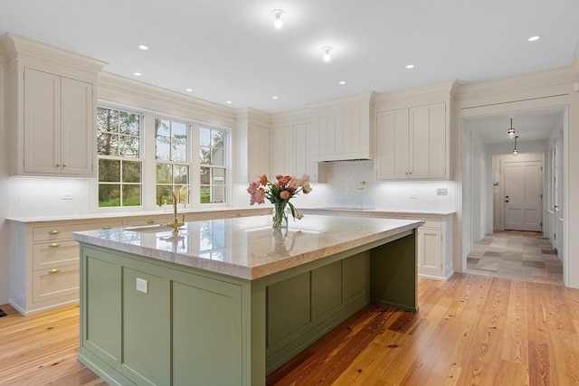 kitchen featuring green cabinetry, a sink, black electric cooktop, light wood-type flooring, and a center island with sink