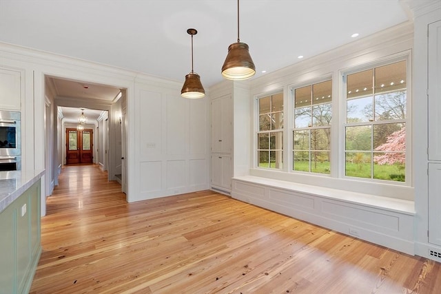 unfurnished dining area featuring ornamental molding, a decorative wall, and light wood-style flooring