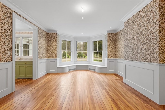 interior space featuring crown molding, wallpapered walls, light wood-style flooring, and a wainscoted wall