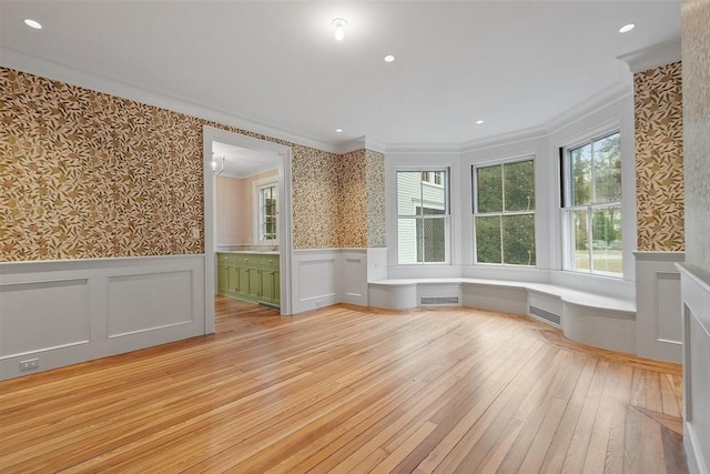 spare room with a wainscoted wall, ornamental molding, wallpapered walls, and light wood-style flooring