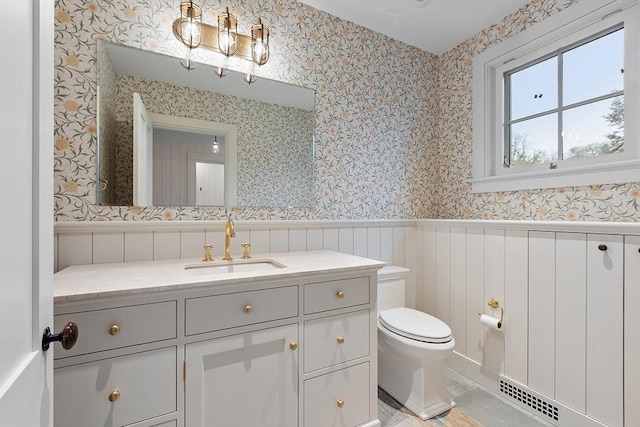 bathroom with visible vents, wainscoting, toilet, and wallpapered walls