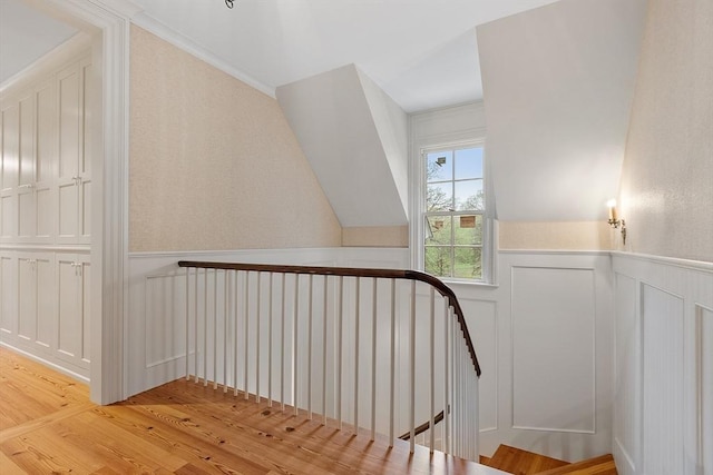 stairway featuring wood finished floors, wainscoting, and a decorative wall