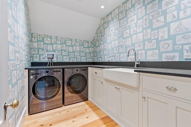 clothes washing area with light wood-style floors, wallpapered walls, washing machine and clothes dryer, a sink, and cabinet space