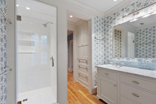 bathroom featuring vanity, a stall shower, wallpapered walls, and wood finished floors