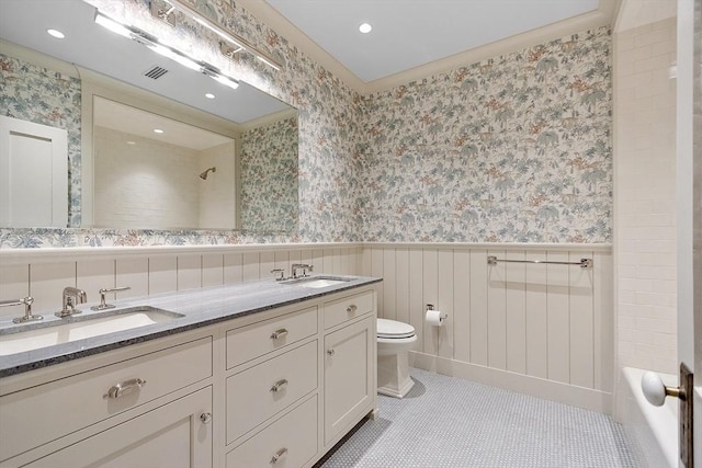 bathroom with a sink, wallpapered walls, wainscoting, and toilet