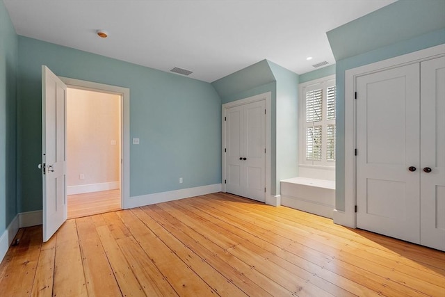unfurnished bedroom with multiple closets, baseboards, light wood-style flooring, and visible vents
