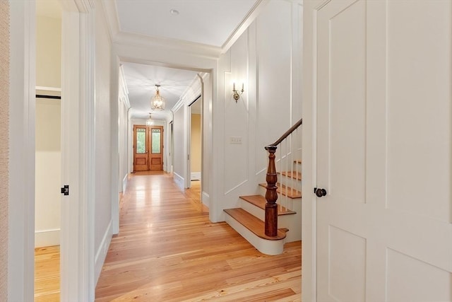 hall with light wood-style floors, baseboards, ornamental molding, and stairway