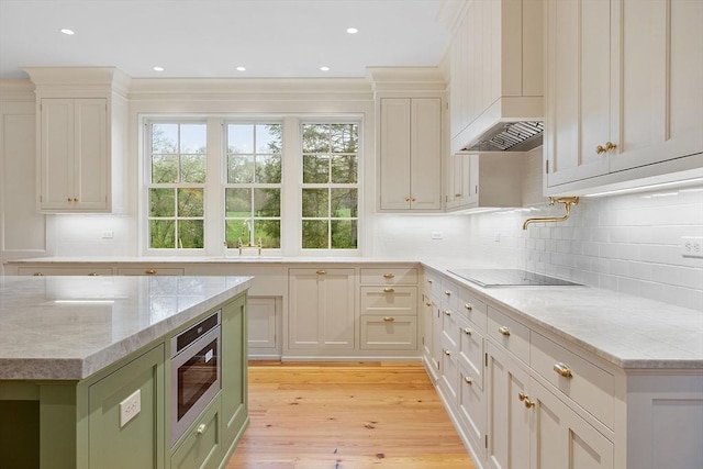 kitchen with decorative backsplash, wall chimney range hood, light wood-type flooring, stainless steel microwave, and a sink