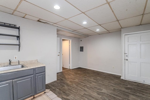 interior space featuring electric panel, a drop ceiling, a sink, and wood finished floors