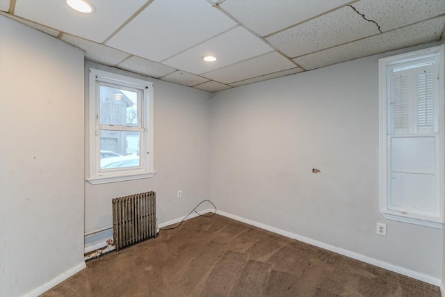 carpeted spare room with baseboards, a drop ceiling, and radiator heating unit