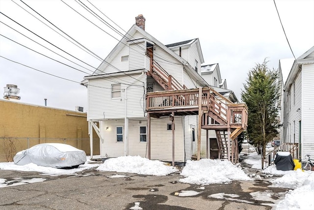 snow covered rear of property with stairway and a chimney