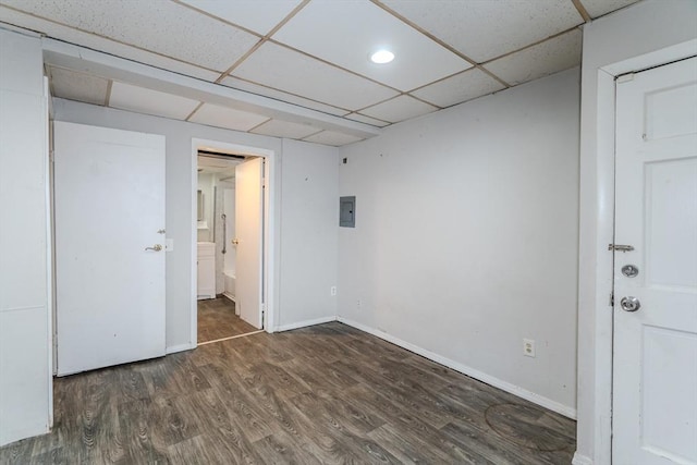 unfurnished room with a drop ceiling, wood finished floors, electric panel, and baseboards