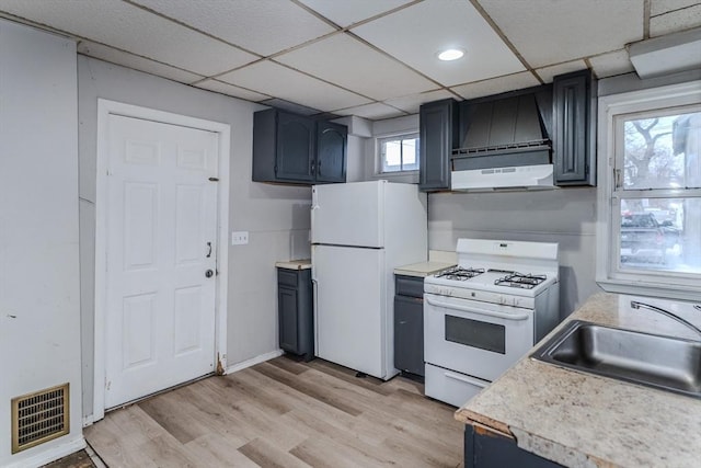 kitchen with under cabinet range hood, white appliances, a sink, visible vents, and light wood-type flooring