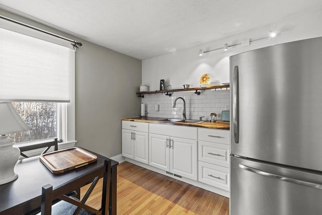 kitchen featuring stainless steel refrigerator, tasteful backsplash, white cabinetry, sink, and light wood-type flooring