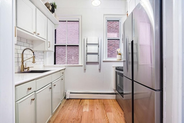 kitchen with light hardwood / wood-style floors, stainless steel appliances, decorative backsplash, a baseboard radiator, and sink