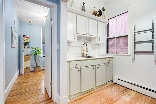 kitchen with light hardwood / wood-style floors, backsplash, a baseboard radiator, white cabinets, and sink