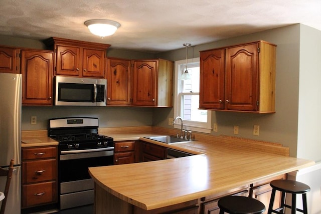 139 Wellman Ave Unit 139, Chelmsford, MA 01863 - kitchen featuring appliances with stainless steel finishes, a peninsula, brown cabinets, and hanging light fixtures