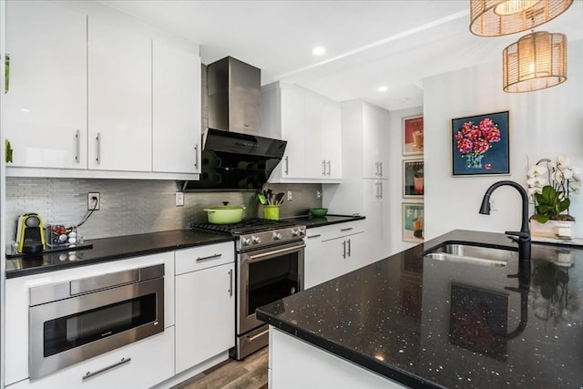 kitchen featuring wall chimney range hood, wood finished floors, a sink, stainless steel appliances, and white cabinetry