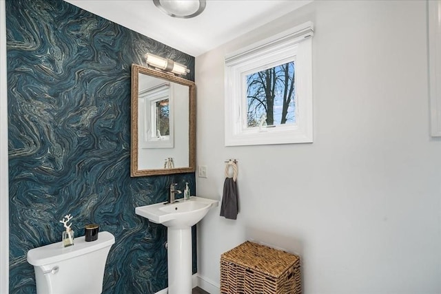 half bath featuring baseboards, toilet, and wallpapered walls