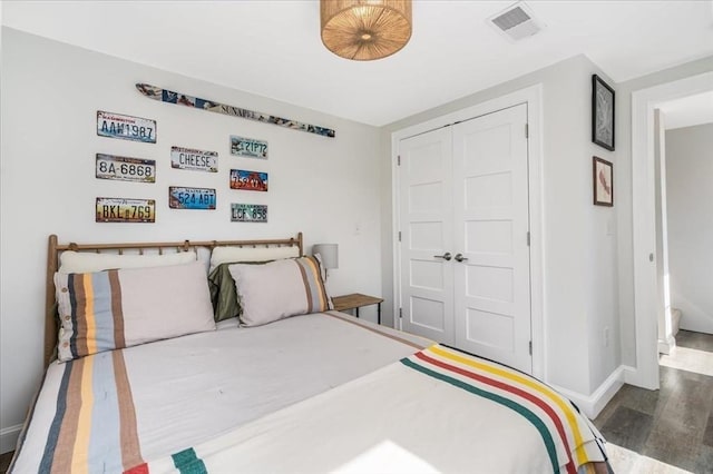 bedroom with baseboards, wood finished floors, visible vents, and a closet