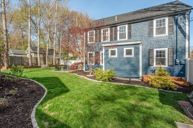 back of property featuring fence, a yard, and roof with shingles