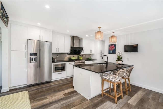 kitchen with high end appliances, dark countertops, dark wood-style floors, wall chimney exhaust hood, and white cabinetry