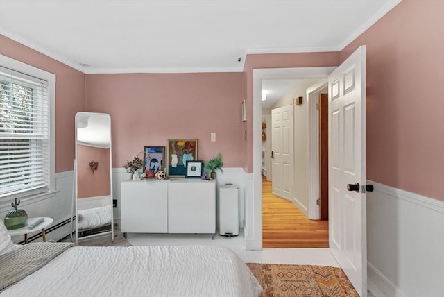 bedroom with a baseboard heating unit, ornamental molding, and a wainscoted wall