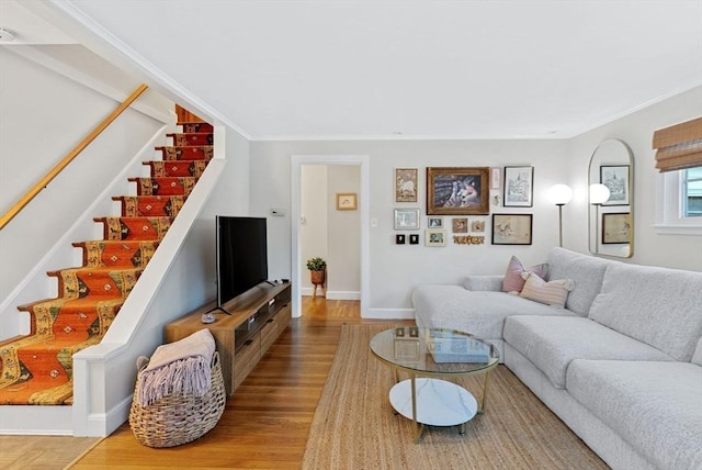 living room featuring light wood-style floors, crown molding, baseboards, and stairs