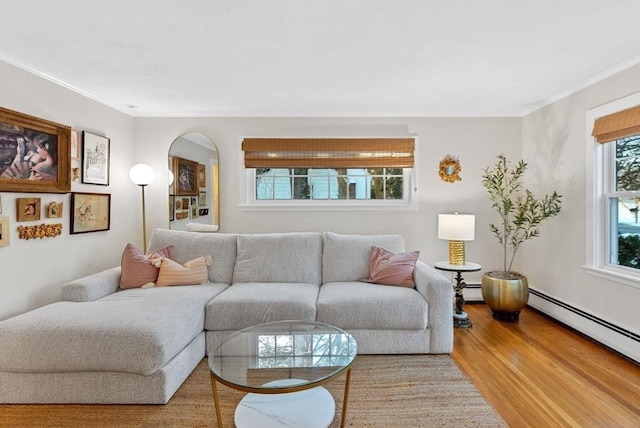 living area with arched walkways, crown molding, baseboard heating, and wood finished floors