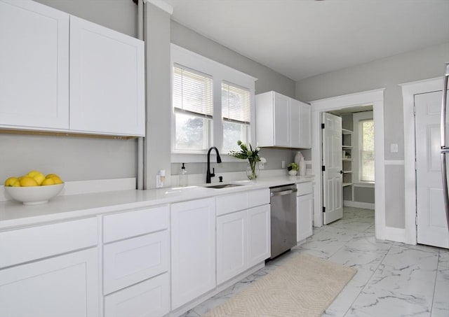 kitchen featuring stainless steel dishwasher, light countertops, marble finish floor, white cabinets, and a sink