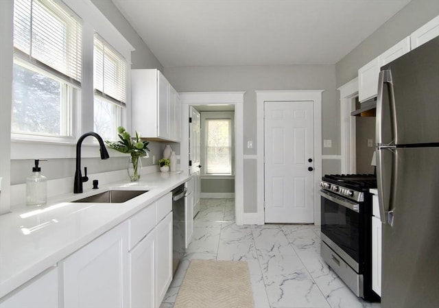 kitchen with a sink, stainless steel appliances, a healthy amount of sunlight, marble finish floor, and white cabinets