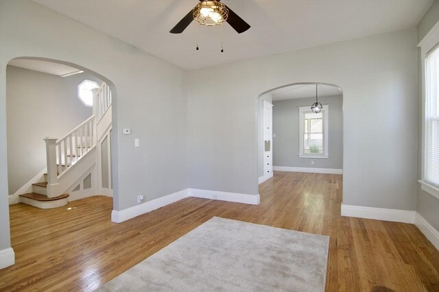 unfurnished room with stairway, wood finished floors, ceiling fan, and arched walkways